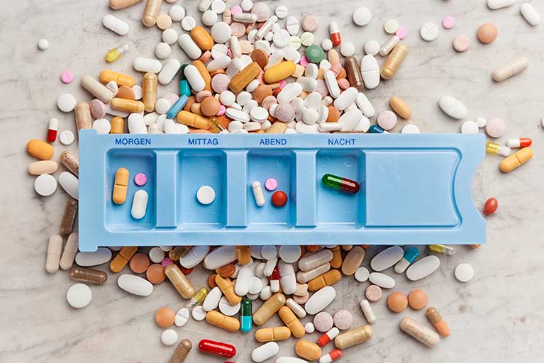 Blaue Pillendose mit vielen bunten Tabletten herum