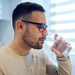 Mann mit Brille trinkt auf einem Wasserglas