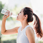 Frau mit Pferdeschwanz trinkt aus Wasserflasche