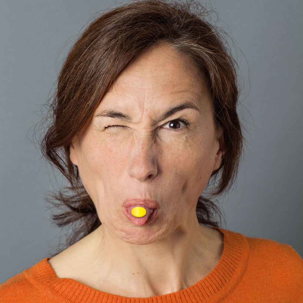 Frau streckt Zunge mit Medcoat auf der Zungenspitze in die Kamera und schaut frech