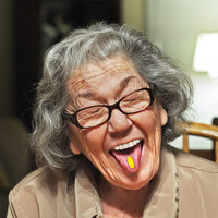 Ältere Dame mit Medcoat auf der Zunge lacht in Kamera und streckt Zunge raus